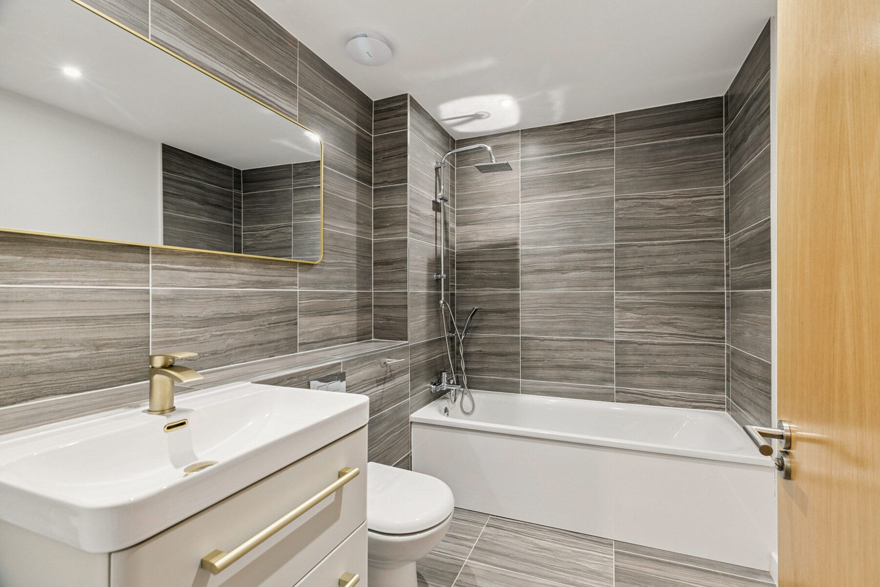 Re-fitted main bathroom with grey stone tiling and brass fixtures