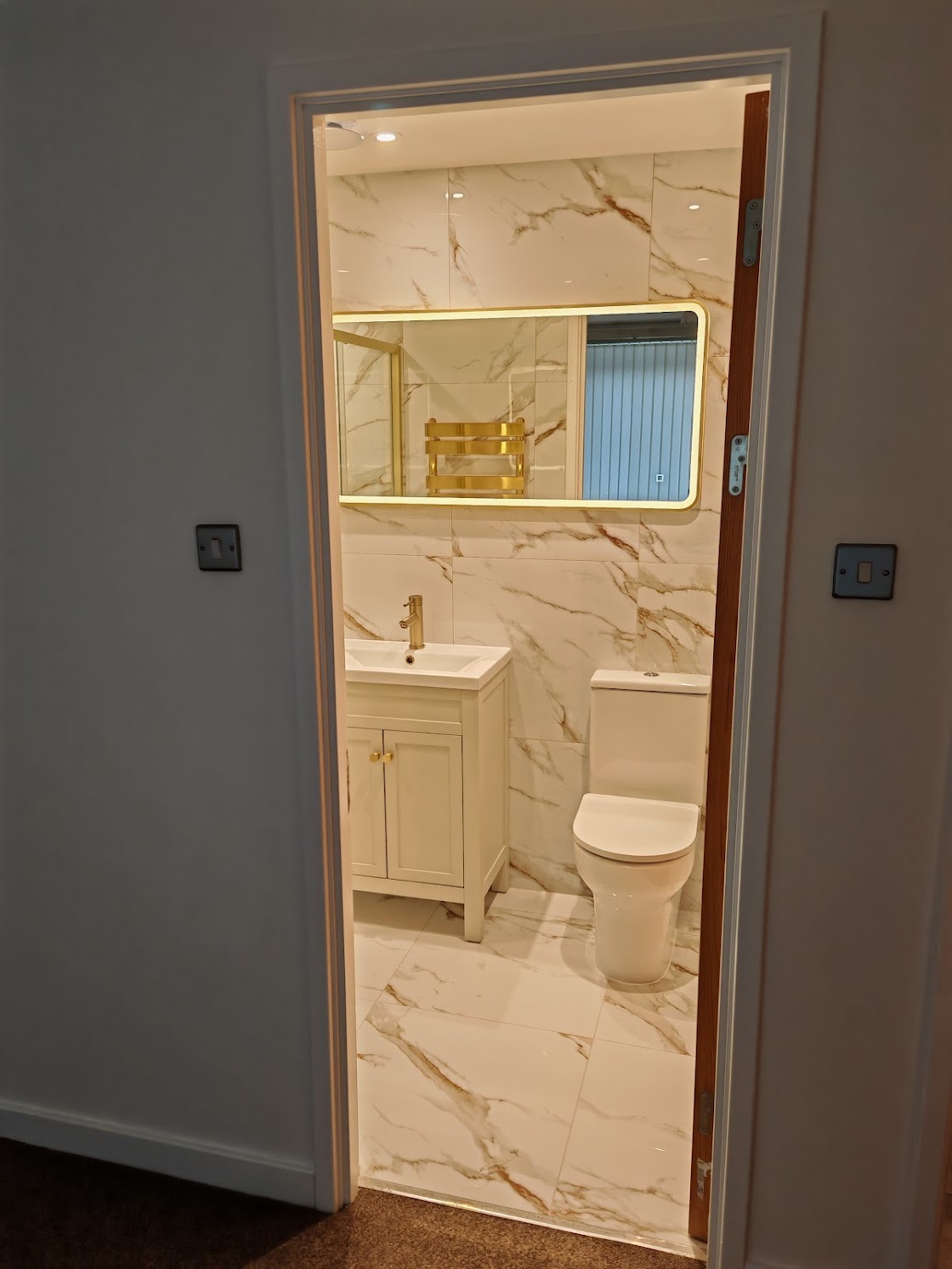 En-suite bathroom showing vanity unit, toilet, LED backlit mirror and gold heated towel rail