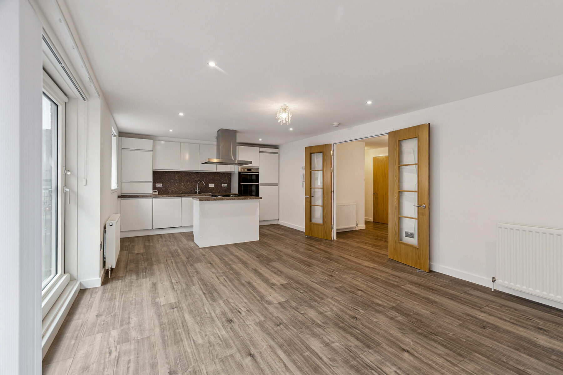 Open-plan living space looking toward the kitchen island with double doors opening to hallway